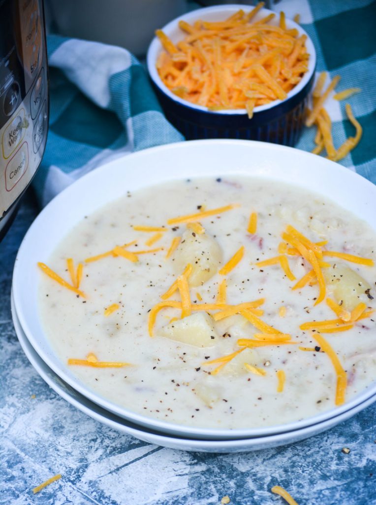 a bowl full of Instant Pot potato soup shown in a white bowl topped with a sprinkle of shredded cheese