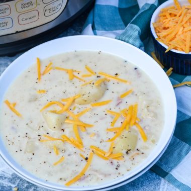 Classic Potato Soup In the Instant pot served in a white bowl with a pressure cooker and a bowl of shredded cheese in the background