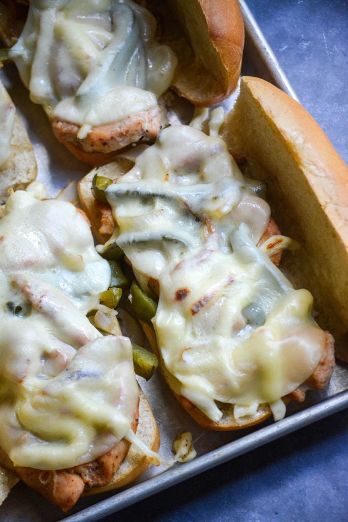 sheet pan philly chicken cheesesteaks assembled on fluffy hoagie rolls set on a sheet pan