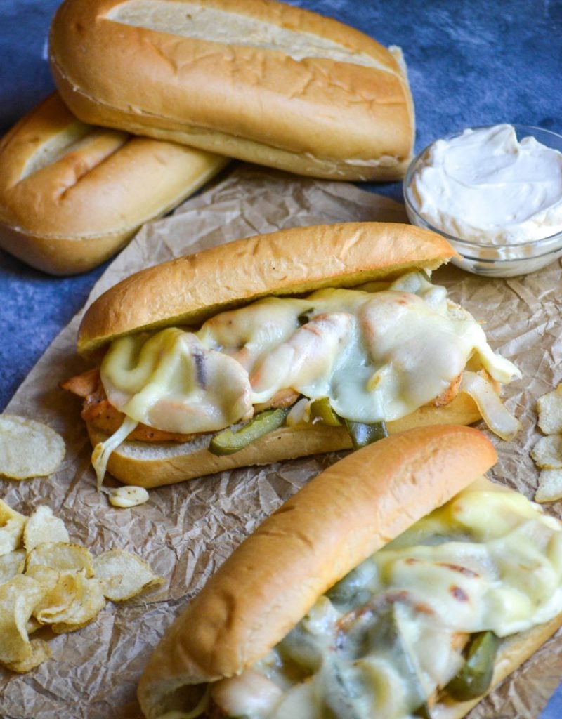extra cheesy philly chicken cheesesteak sandwiches shown on wrinkled brown parchment paper