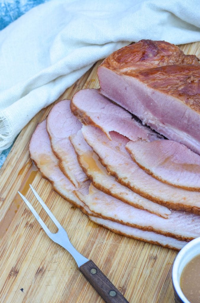 crockpot glazed ham shown sliced on a wooden cutting board and drizzled with juices