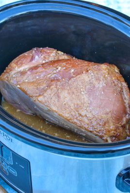 a ham in the black bowl of a crockpot with a maple Dijon glaze poured over it