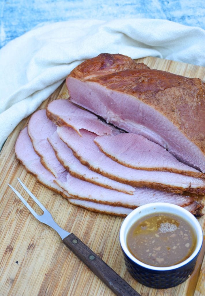 crockpot glazed ham sliced and served on a wooden cutting board with a meat fork