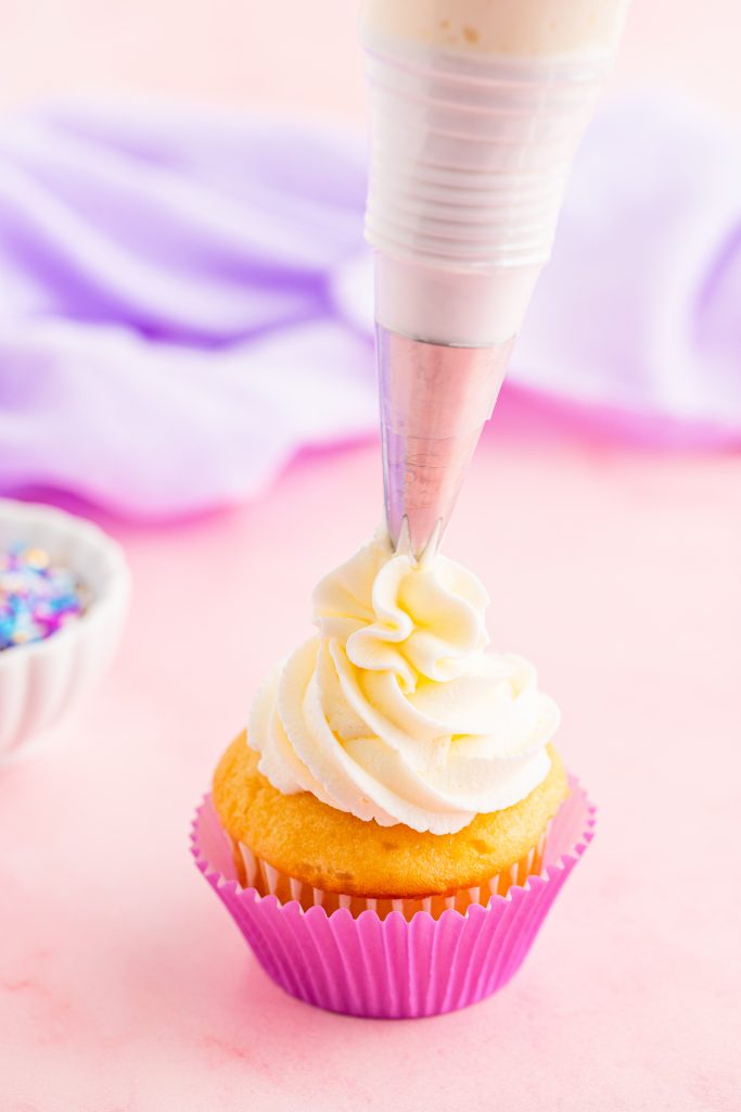 cake decorating frosting shown being piped onto a yellow cupcake