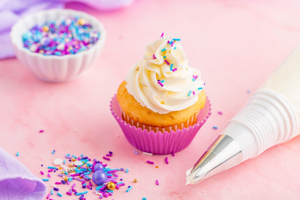 vanilla buttercream frosting shown in a fluffy mound on a yellow cupcake topped with colored sprinkles