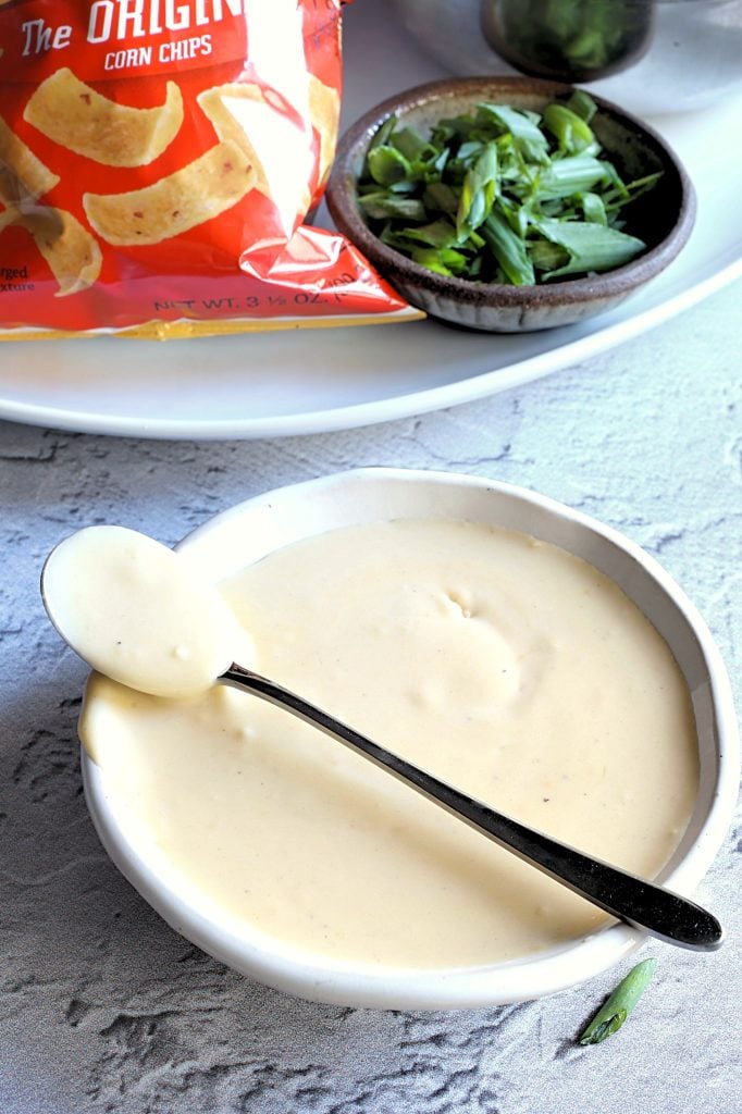 cheese sauce shown in a white bowl with a silver spoon resting on top