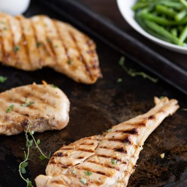 grilled teriyaki chicken on a black sheet pan with fresh herbs and sauce for dipping