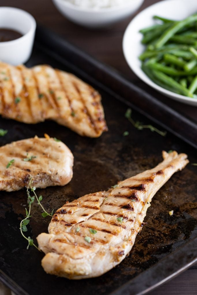 grilled teriyaki chicken on a black sheet pan with fresh herbs and sauce for dipping