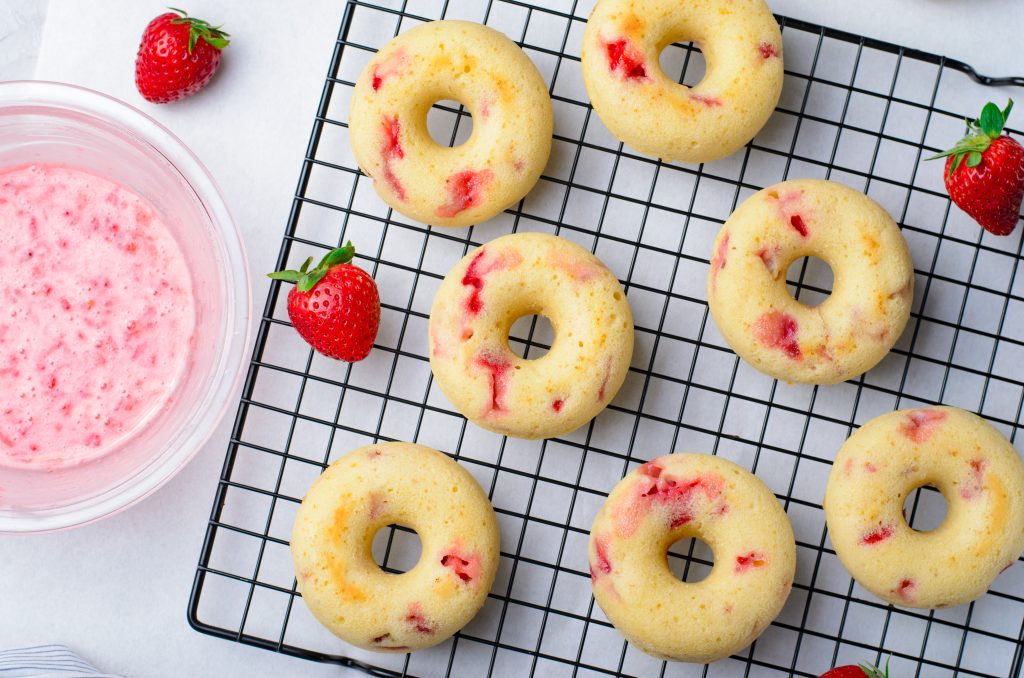 baked strawberry donuts shown on a metal cooling wrack