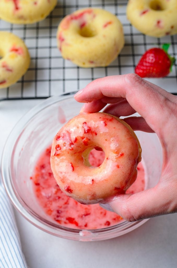 a hand holding up a freshly glazed strawberry donut