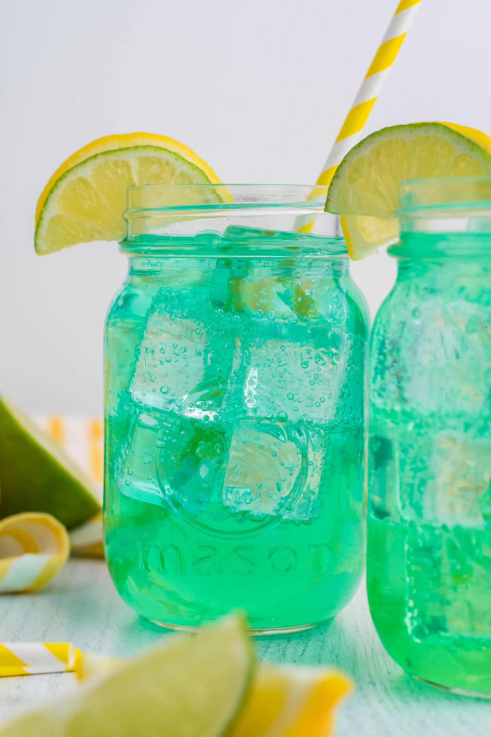 the best copycat baja blast recipe served over ice in clear glass jars with stripped yellow straw and sliced lemons for garnish