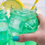 a hand holding up a glass filled with copycat baja blast soda recipe over ice