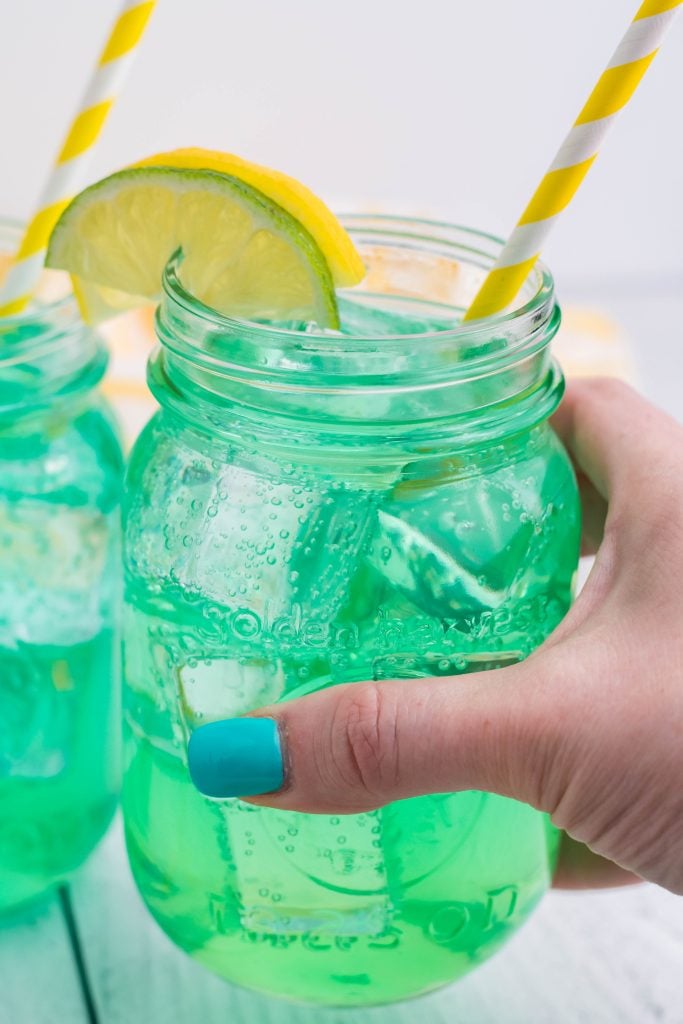 a hand holding up a glass filled with copycat baja blast soda recipe over ice