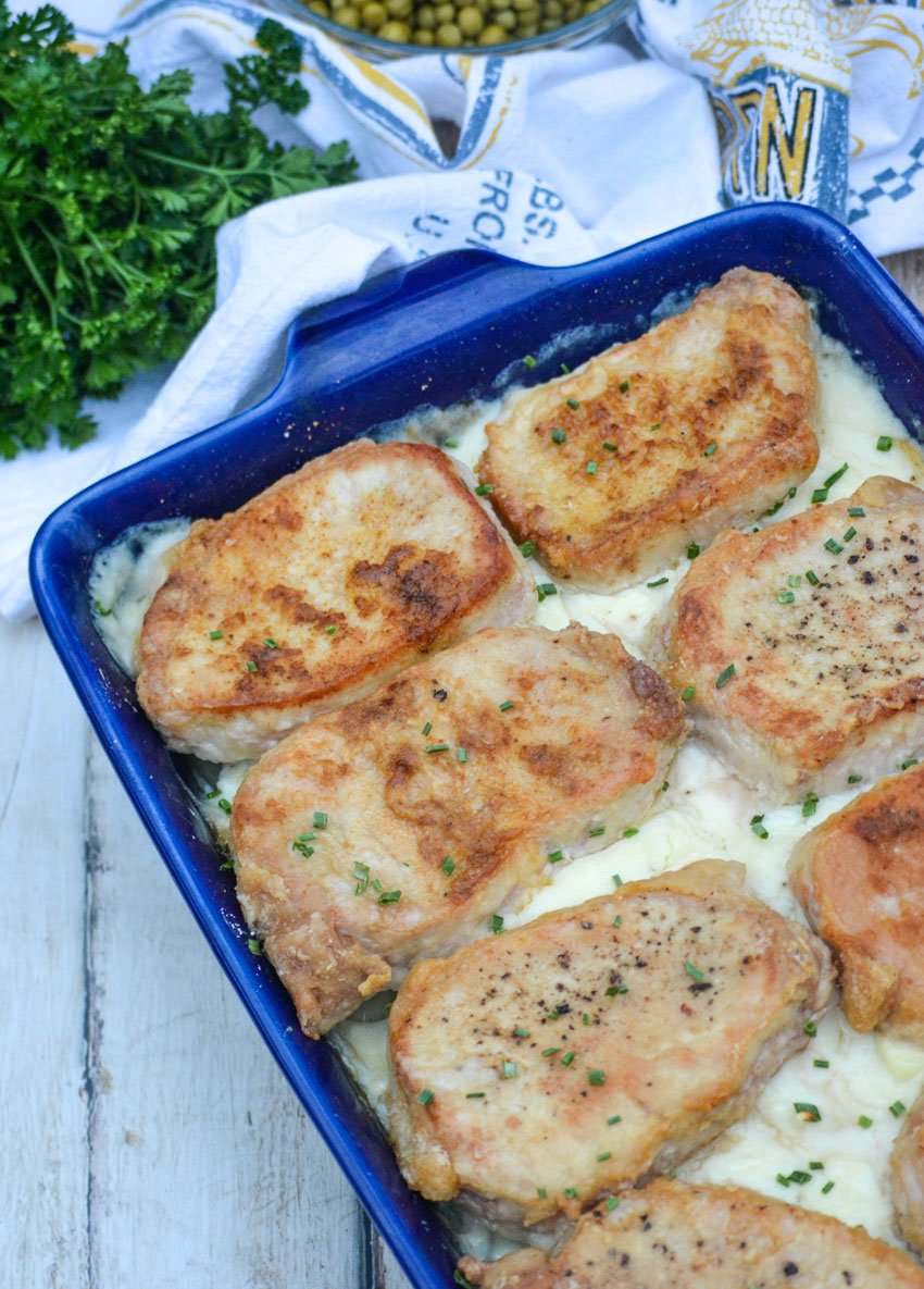 thick Farmer's style pork chops over a bed of creamy scalloped potatoes in a blue casserole dish