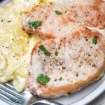 baked pork chops and potatoes on a white dinner plate with a silver fork resting on the side