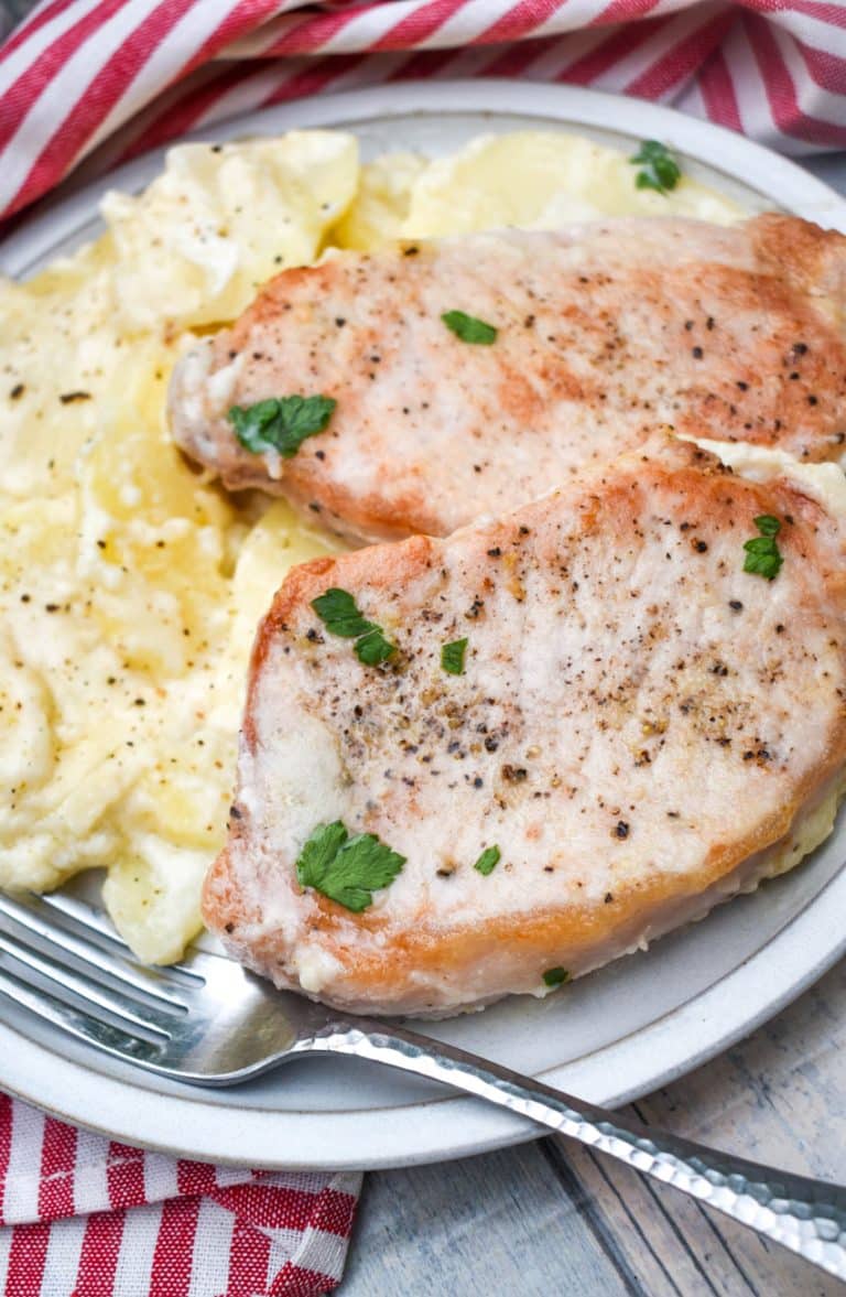 baked pork chops and potatoes on a white dinner plate with a silver fork resting on the side