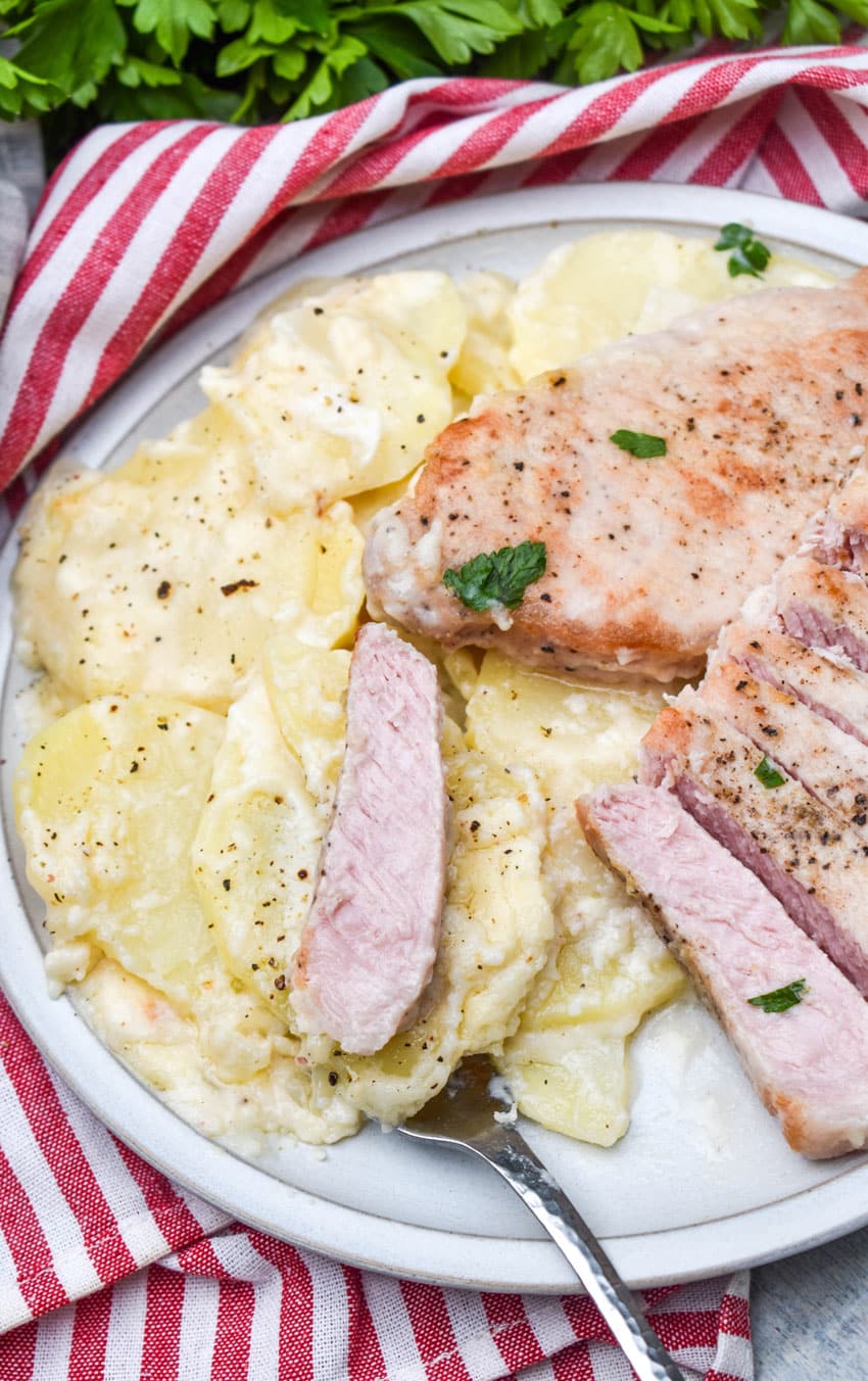 baked pork chops and potatoes on a white dinner plate with a silver fork resting on the side