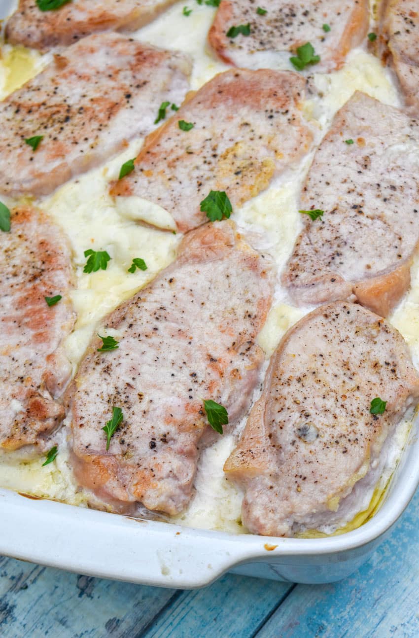 baked pork chop and potatoes in a white casserole dish topped with fresh chopped green herbs