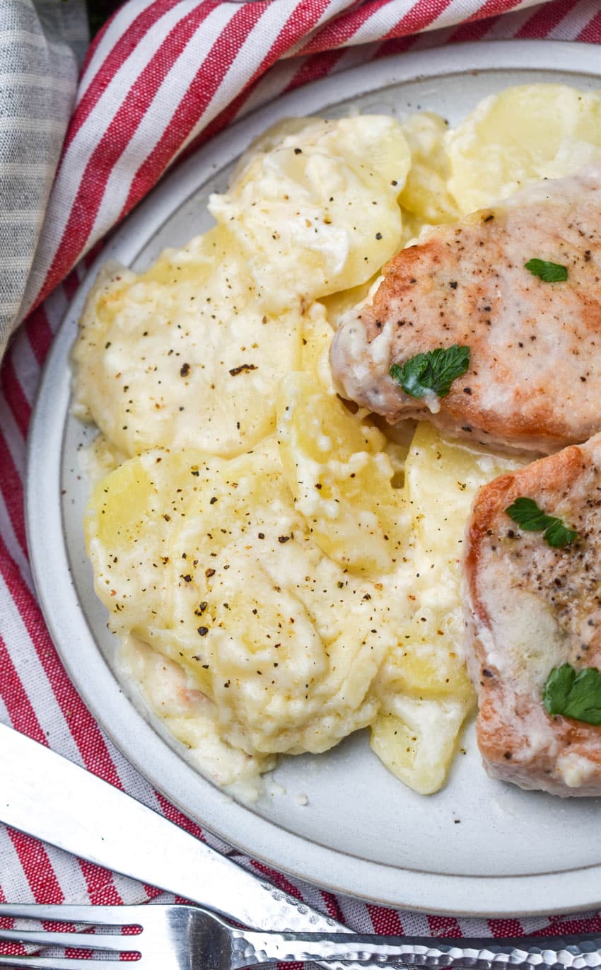 creamy baked potatoes next to baked pork chops on a small gray dinner plate