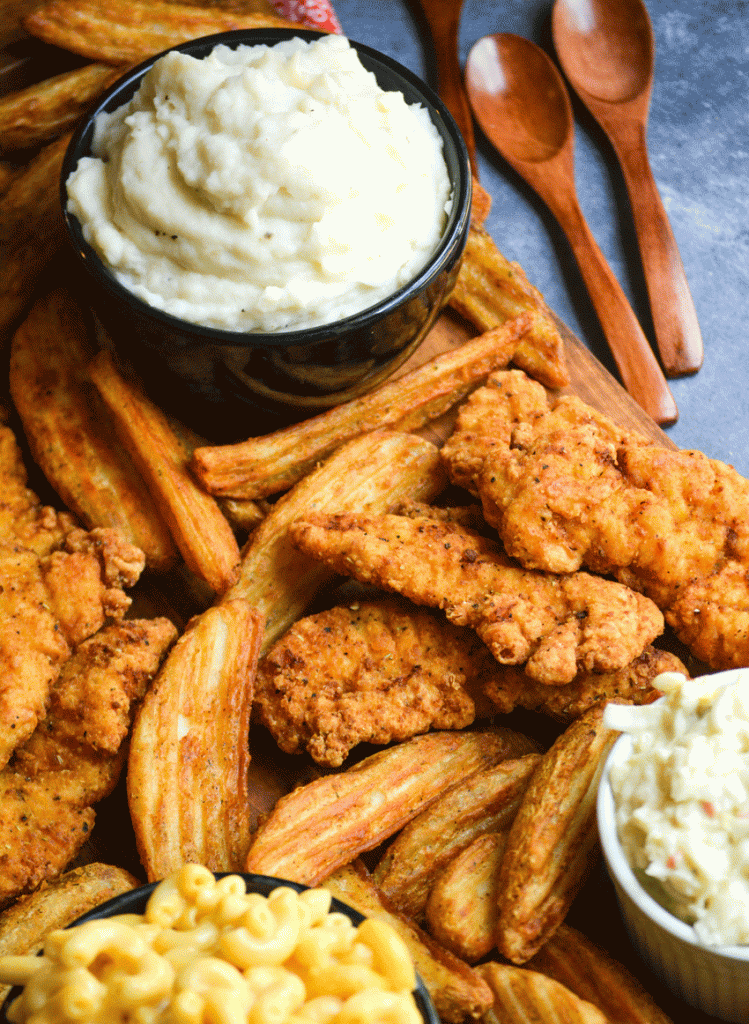 a fried chicken dinner arranged on a rectangular wooden serving board