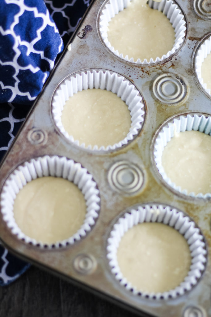 cupcake batter shown in white cupcake liners in a muffin tin ready to be baked