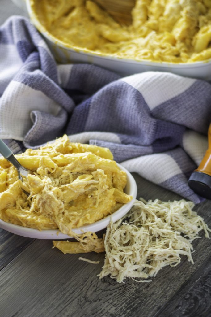 baked buffalo chicken mac and cheese shown in a white bowl with a fork stuck in it with a patterned cloth napkin and casserole dish in the background