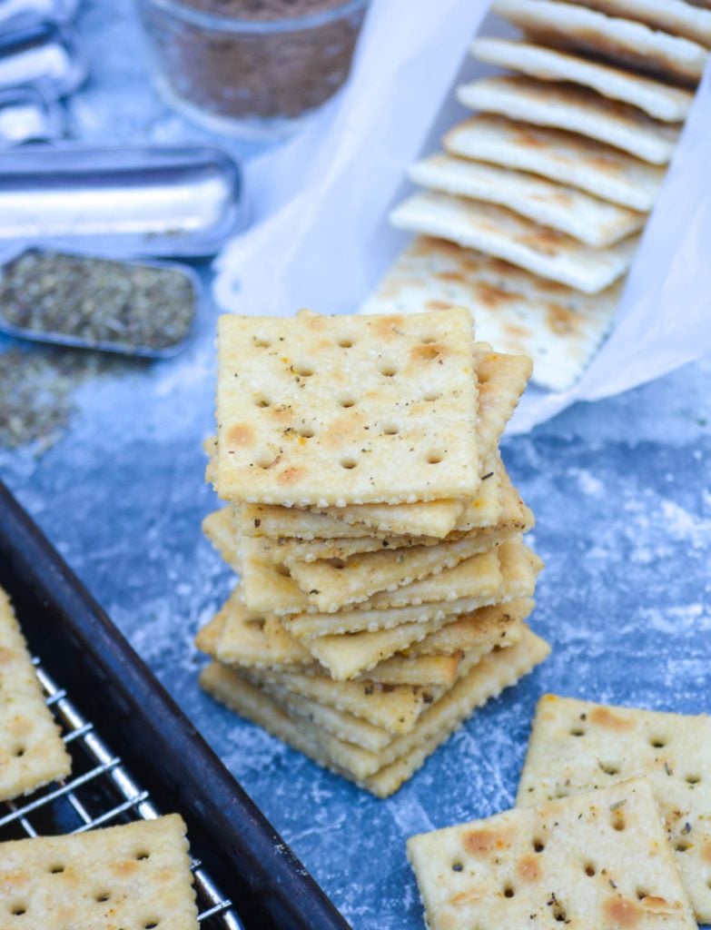 a stack of savory Italian seasoned saltine crackers shown in the center or a blue counter with all of the ingredients staged evenly around them
