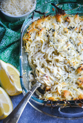 a silver spoon shown scooping some creamy lemon chicken spaghetti bake from a glass dish