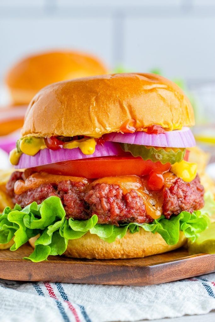 a smoked burger shown in a fluffy bun piled high with vibrant, fresh fixings and served on a wooden cutting board