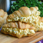 three croissants stuffed with the best basic egg salad stacked together on a wooden cutting board