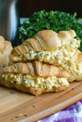 three croissants stuffed with the best basic egg salad stacked together on a wooden cutting board