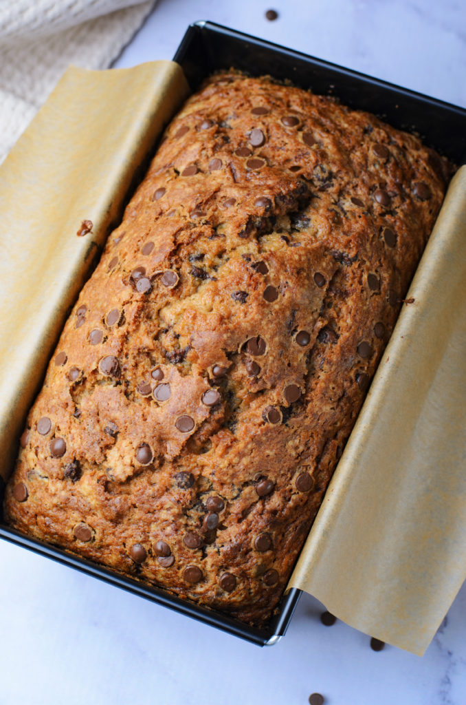 a loaf of chocolate chip zucchini bread shown on a piece of brown parchment paper overlapping a metal loaf pan