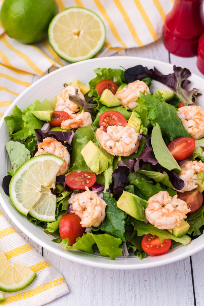 brightly colored fiesta lime shrimp salad shown in a white bowl garnished with fresh lime slices