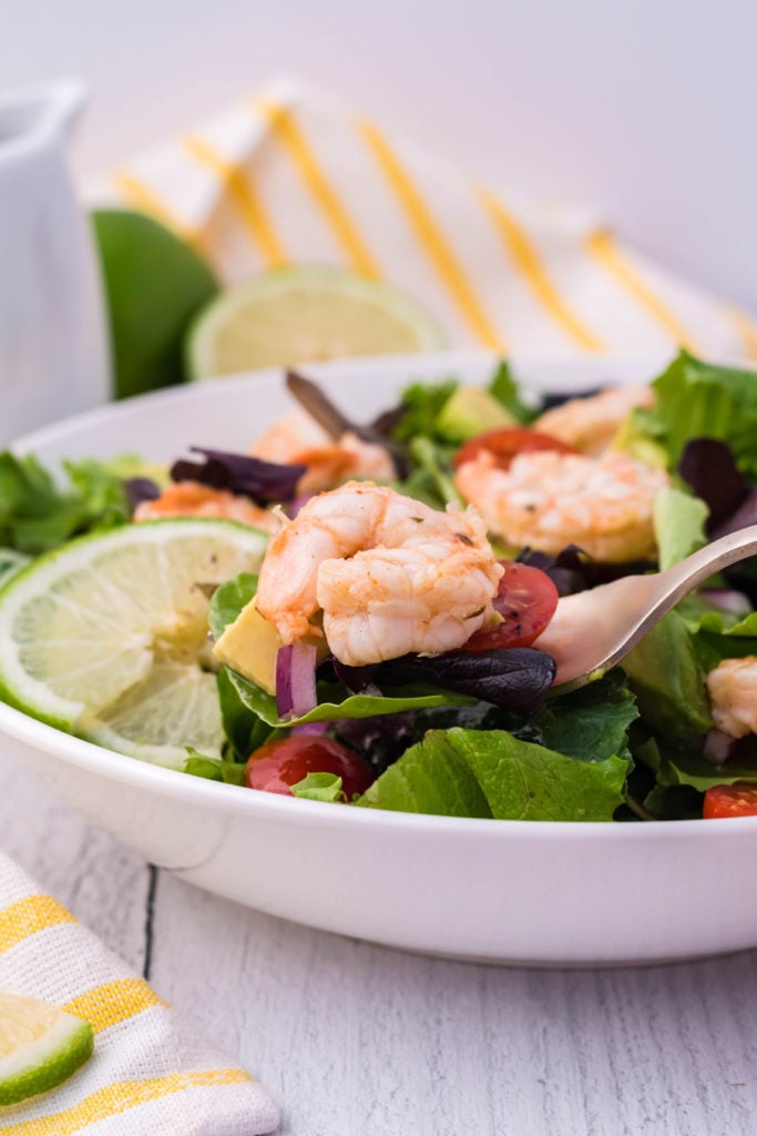 a silver fork shown with fiesta lime shrimp held over a bowl of salad greens