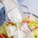 homemade ranch dressing being poured from a glass jar onto a waiting salad