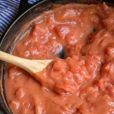 a wooden spoon shown stirring tomato gravy in a black cast iron skillet