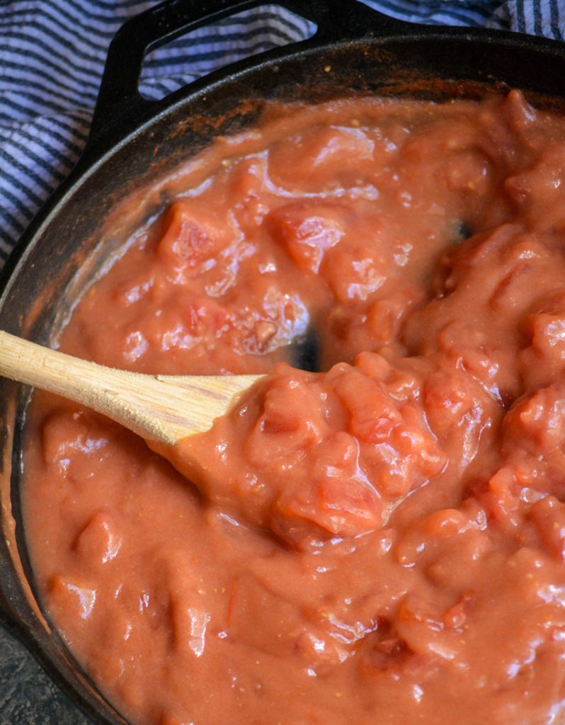 a wooden spoon shown stirring tomato gravy in a black cast iron skillet