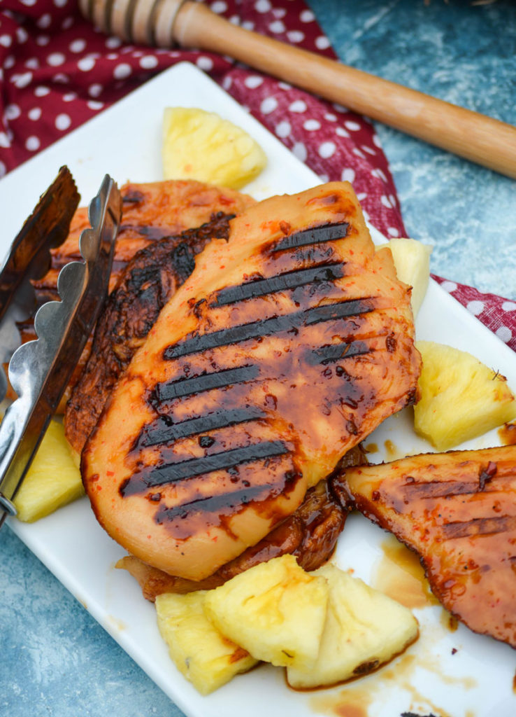 grilled pineapple chicken shown on a white platter with chunks of fresh pineapple and a pair of silver tongs