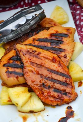 grilled pineapple chicken shown on a white platter with chunks of fresh pineapple and a pair of silver tongs