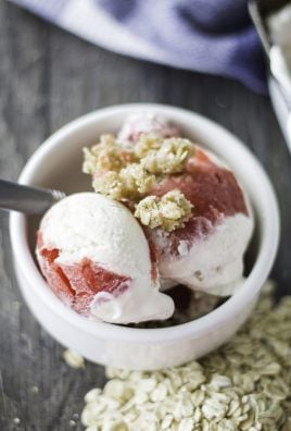 scoops of no churn cherry cobbler ice cream shown in a white bowl with a silver spoon and streusel topping