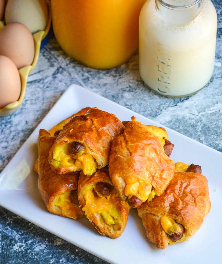sausage egg and cheese breakfast rolls shown on a white platter with eggs and juice in the background