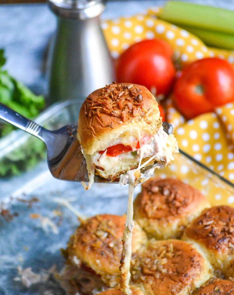 a silver spatula holding up a tuna melt slider with tendrils of melted cheese hanging down