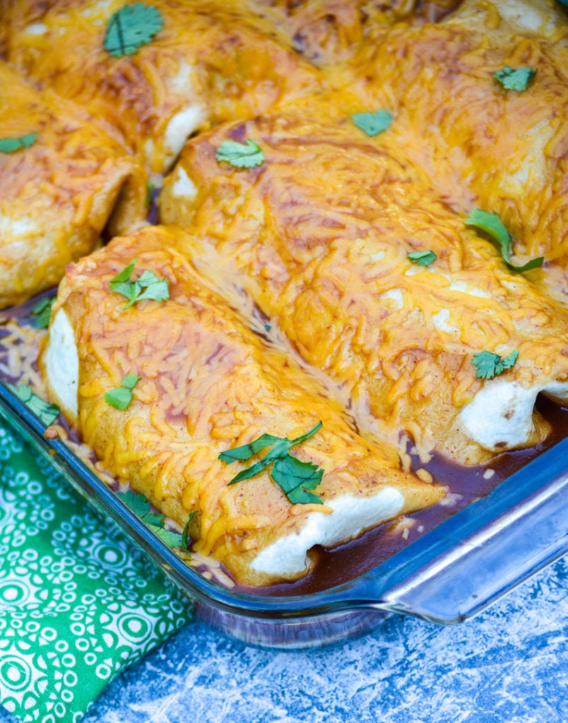 wet burritos smothered with sauce and cheese shown in a glass baking dish