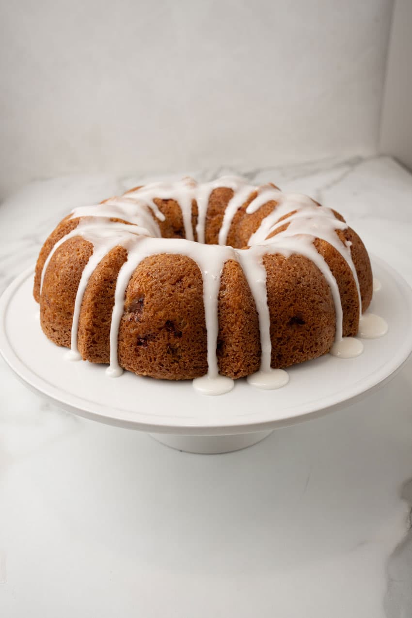 a strawberry lemon yogurt cake drizzled with powdered sugar glaze on a white cake stand