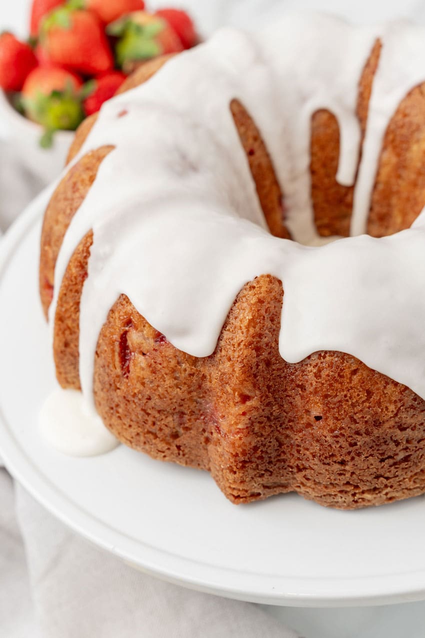 a glazed strawberry lemon yogurt cake on a white cake stand