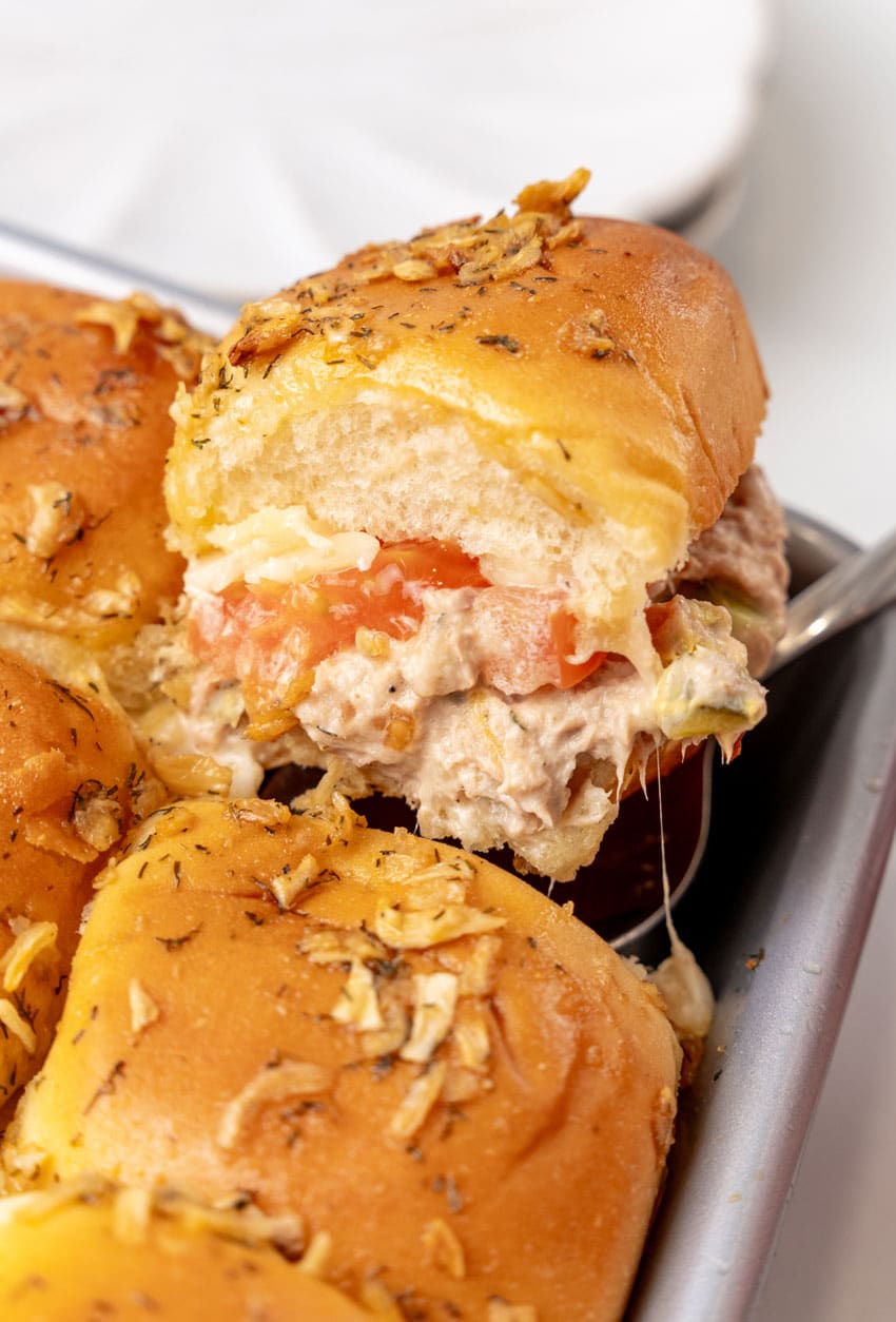 a silver spatula lifting a tuna melt slider out of of a metal baking dish