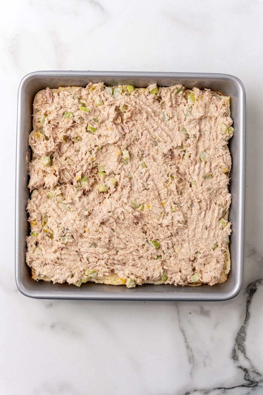 tuna salad mixture spread over slider buns in a square metal baking dish