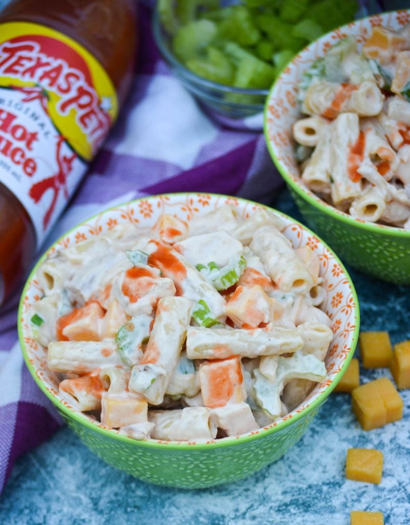 buffalo chicken pasta salad shown served in small green bowls with a drizzle of hot sauce