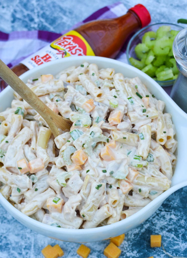 a wooden spoon shown scooping buffalo chicken pasta salad out of a large white bowl