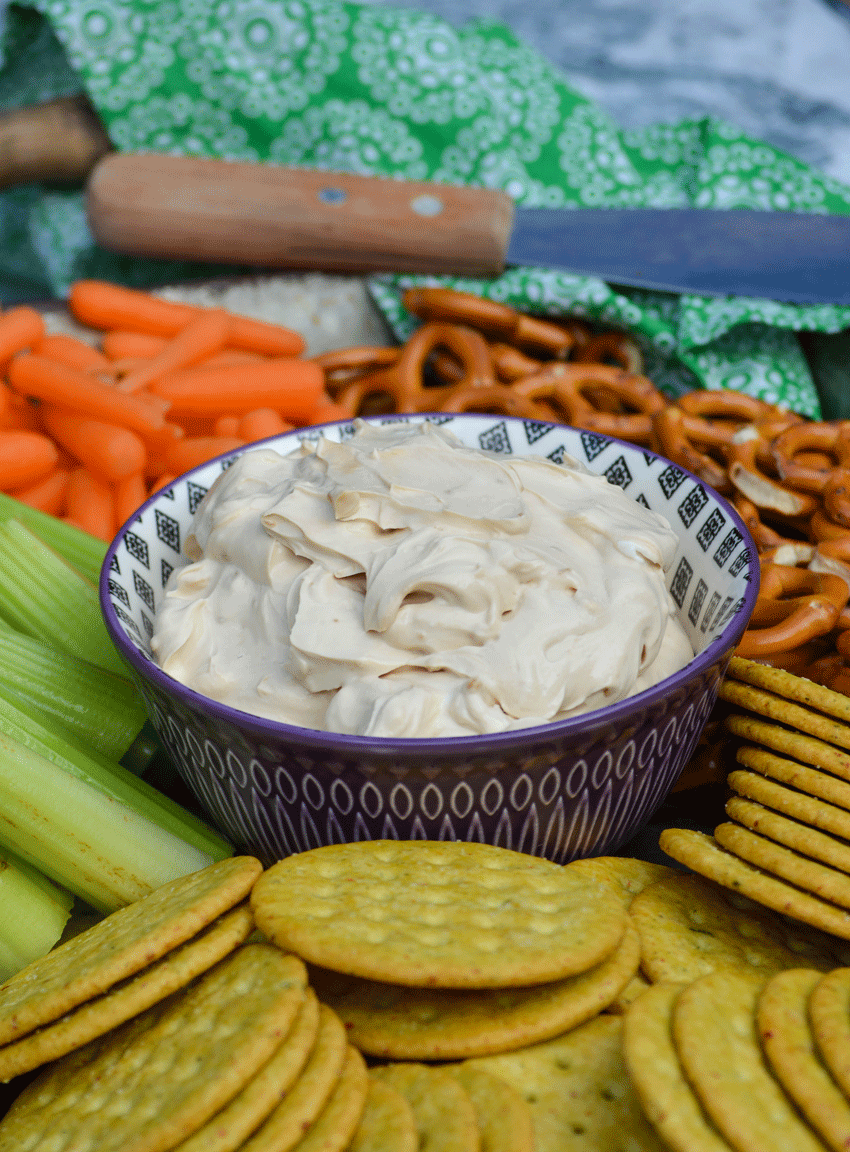 creamy french onion dip in a small purple bowl and surrounded by vegetables and crackers